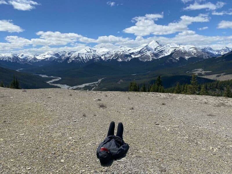 Person lying on ground with mountains and sky in background.