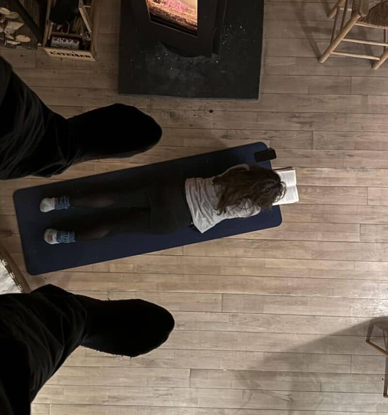 Person lying on a blue mat reading a book in a cozy room.