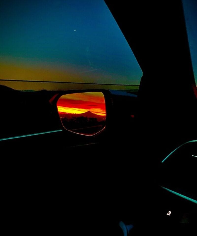 Sunset view seen through car side mirror with colorful sky and horizon.
