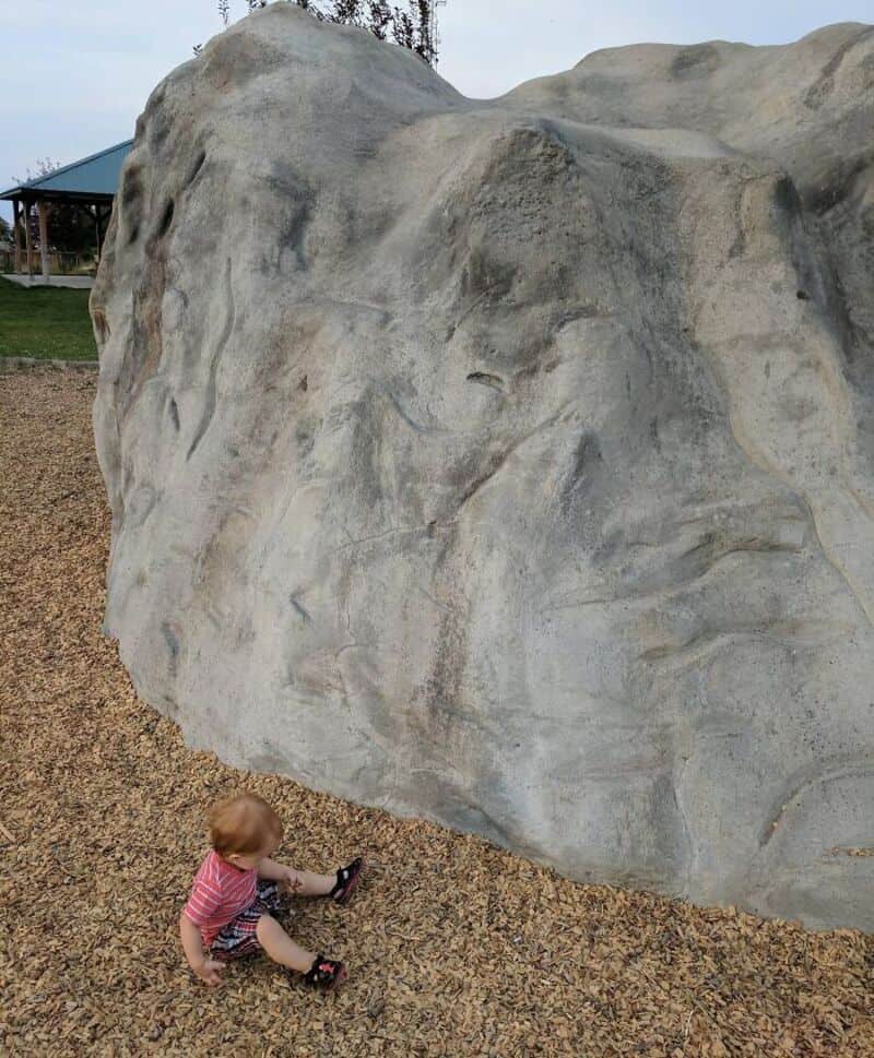 Child sitting near a large, unusual rock formation at a park.
