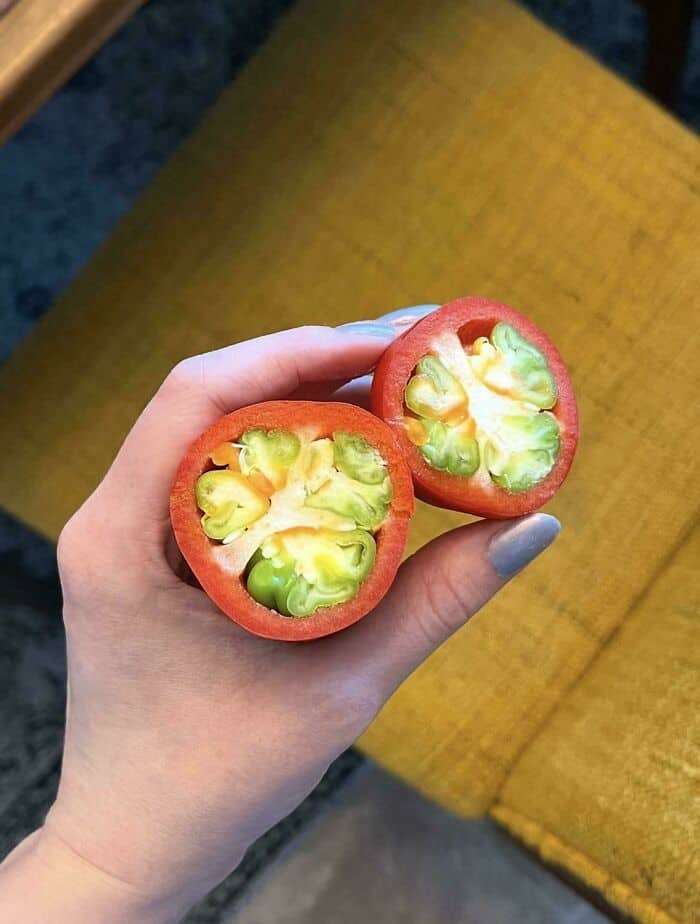 Hand holding a tomato cut in half showing unusual green and yellow interior.
