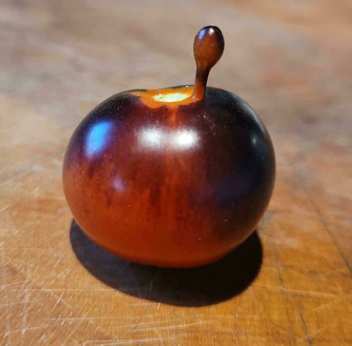 A small, round, dark red fruit with a stem on a wooden surface.