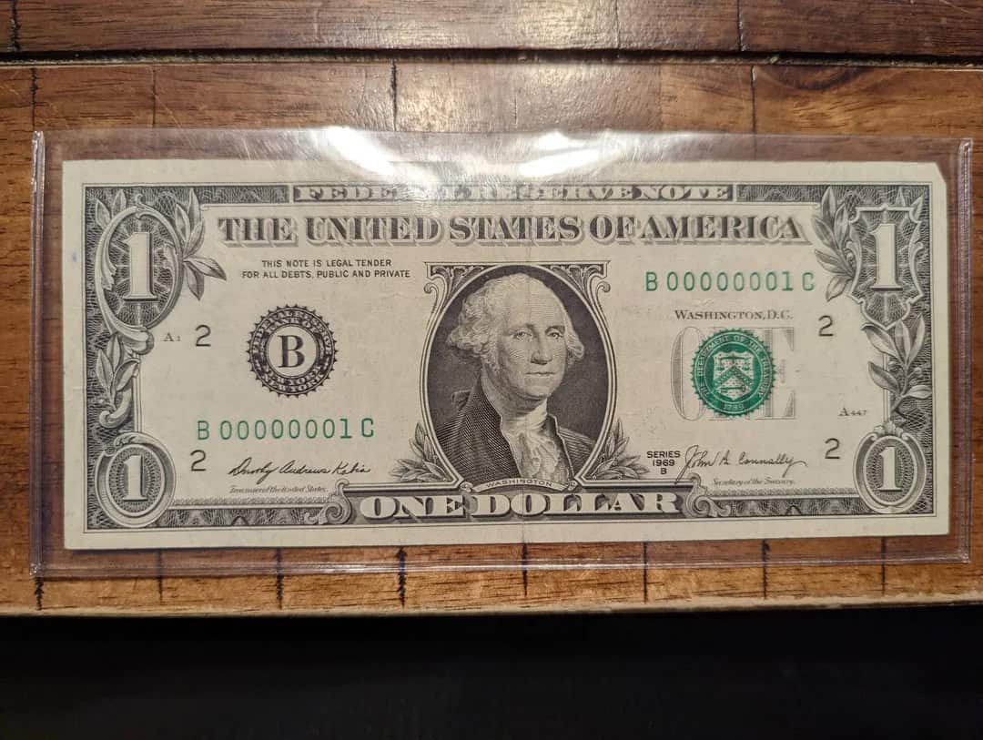 One dollar bill framed on a wooden background.