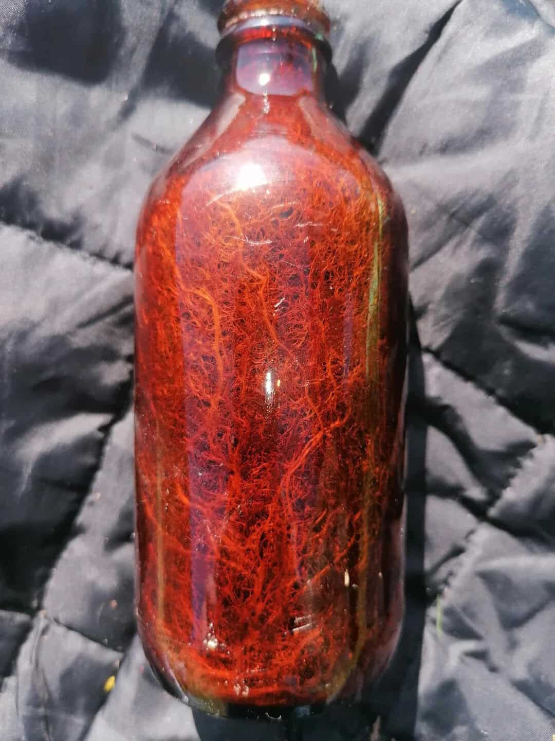 A glass bottle with a reddish-brown, web-like pattern on its surface.