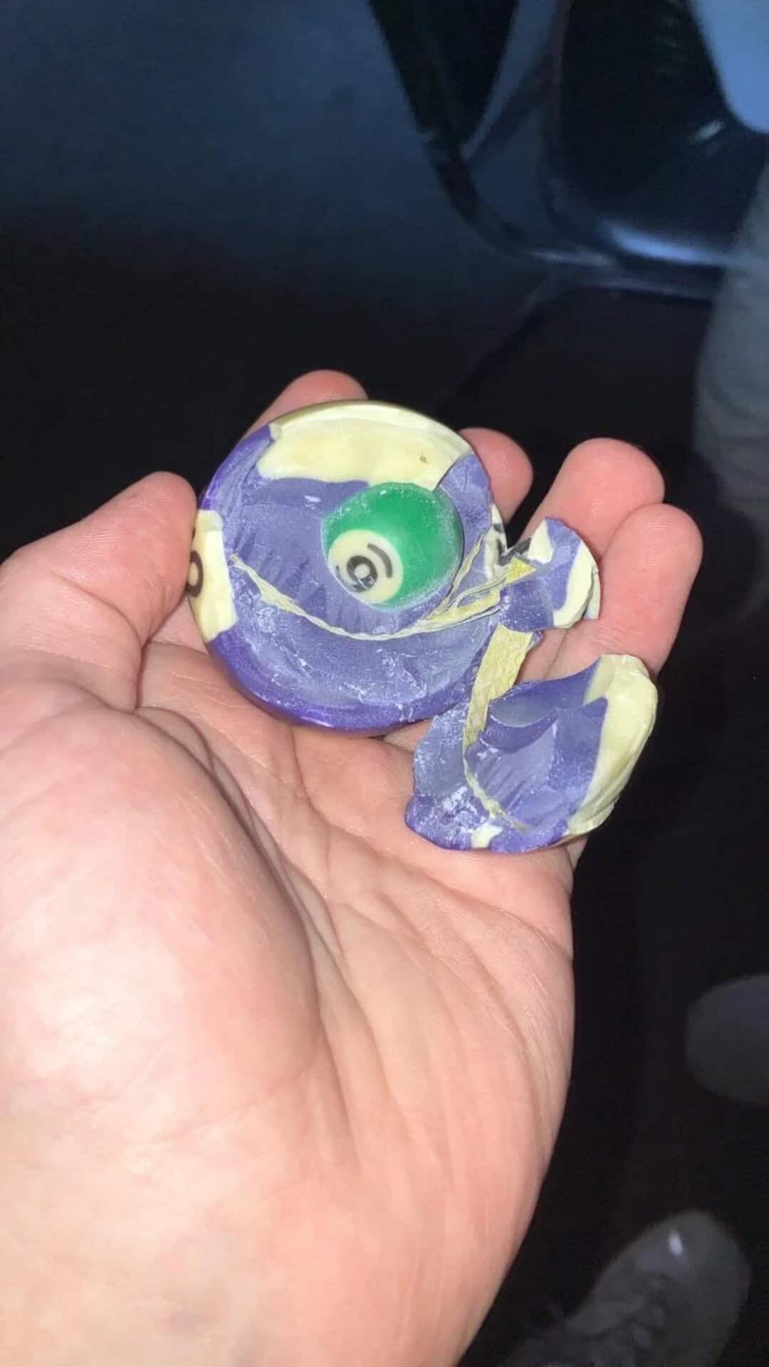 Colorful marble inside a small, purple and yellow ceramic teapot-shaped container.