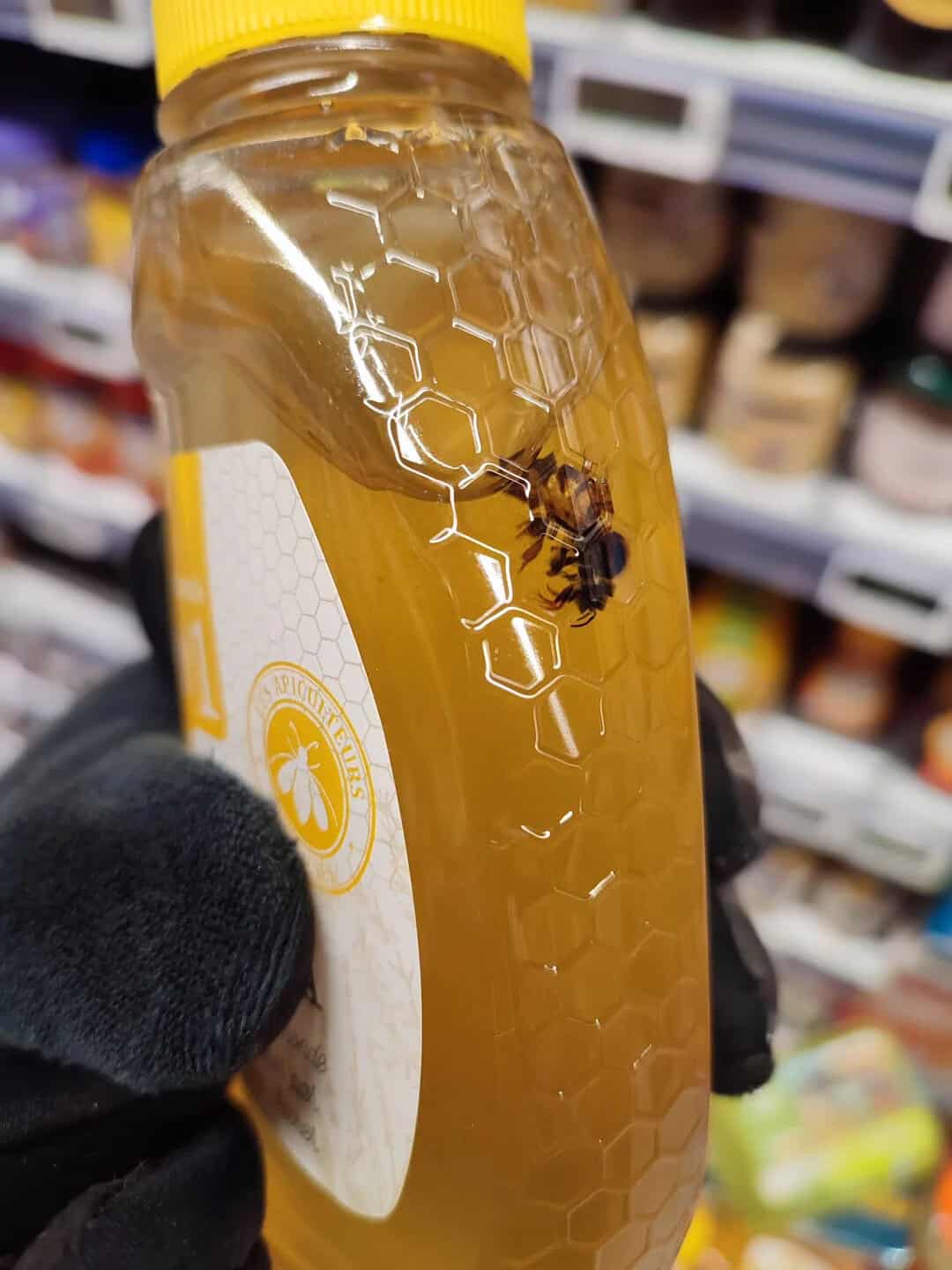 Honey jar with a bee on the honeycomb pattern, store shelves in the background.