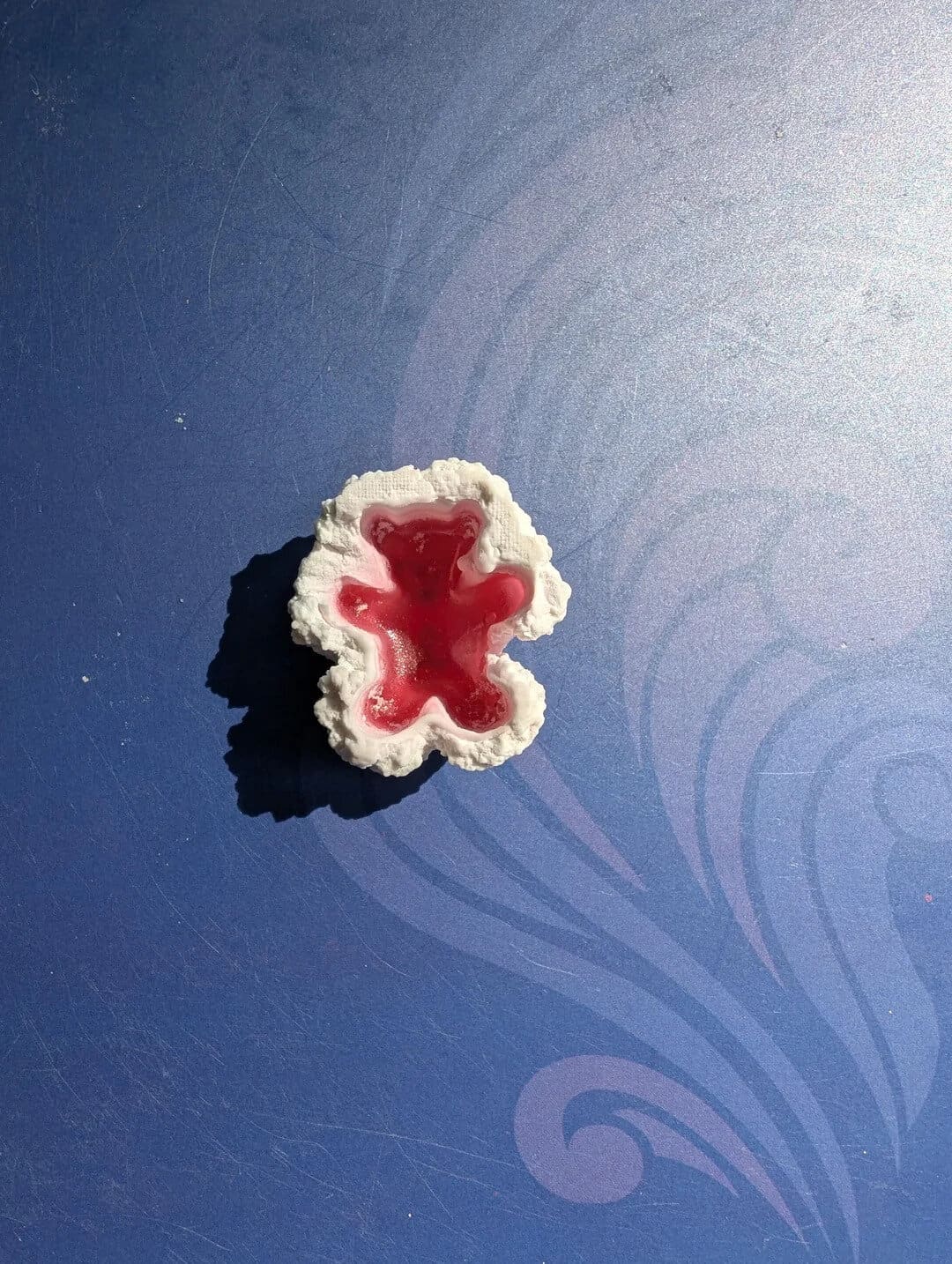 Gummy bear-shaped gummy candy with red filling on a blue surface.