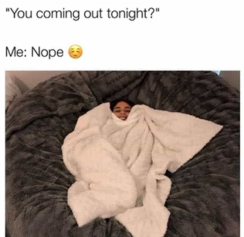 Person wrapped in a white blanket on a dark gray couch, smiling.