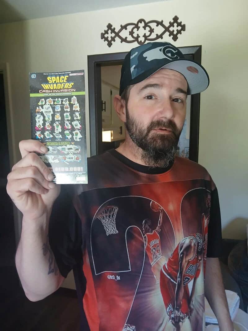 SPACE INVADERS scratch-off lottery ticket held by man in casual clothing and cap.