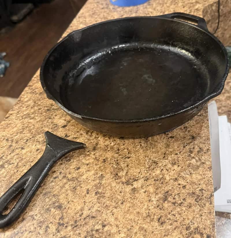 Cast iron skillet with handle on a brown countertop, with some oil residue inside.