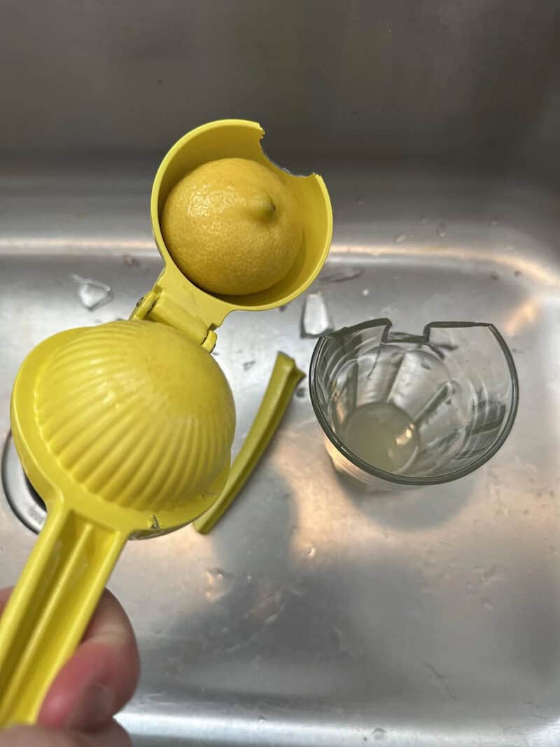 Lemon in a yellow citrus juicer over a sink with a glass of lemon juice.