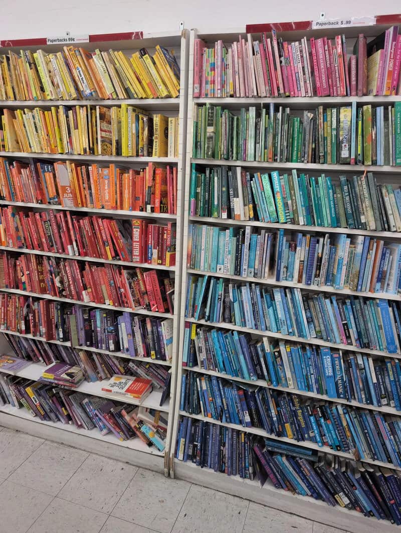 Rainbow-colored bookshelves with books arranged by color in a library.