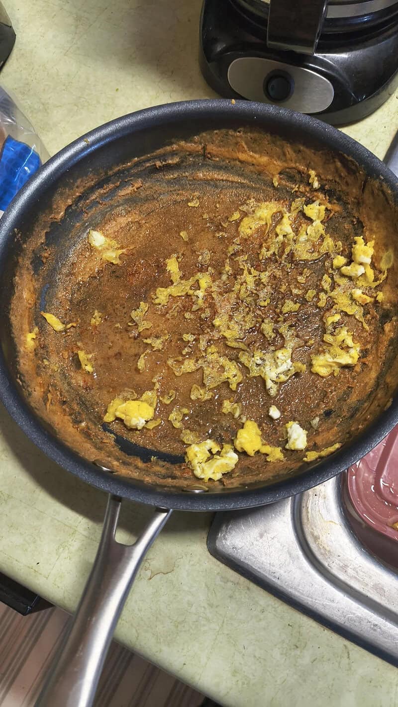 Scrambled eggs in a non-stick frying pan with some browned areas.