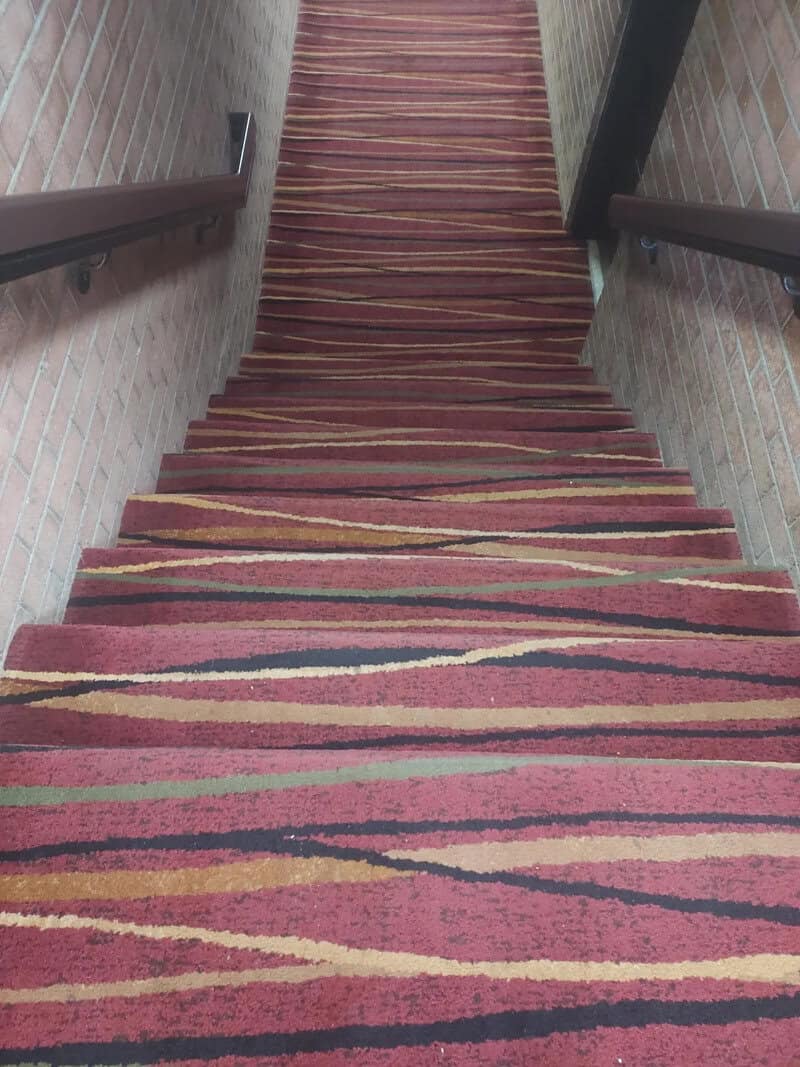 Carpeted staircase with a colorful striped pattern and brick walls on both sides.