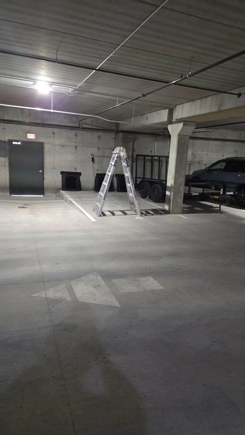 Indoor parking garage with a ladder and parked cars under a concrete ceiling.