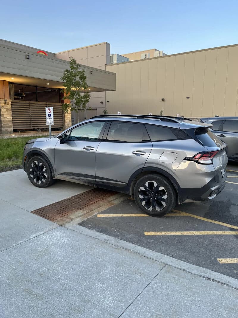Silver SUV parked in a lot near a building with a tree and a "No Parking" sign.