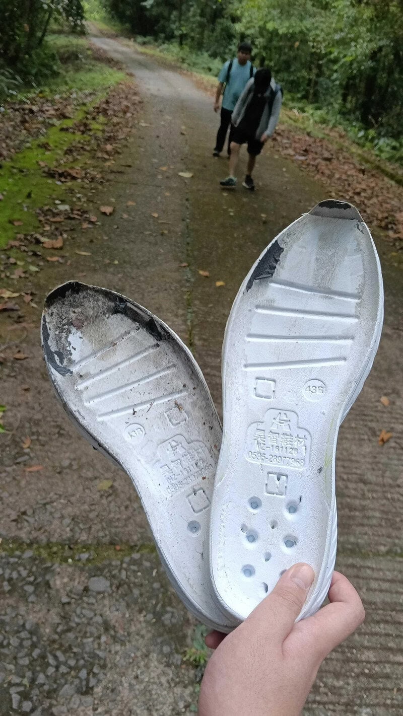 Worn silver shoe insoles held up on a trail with two hikers in the background.