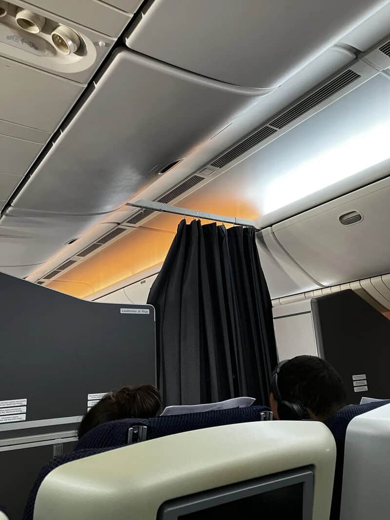 Airplane cabin interior with black curtains and overhead compartments.