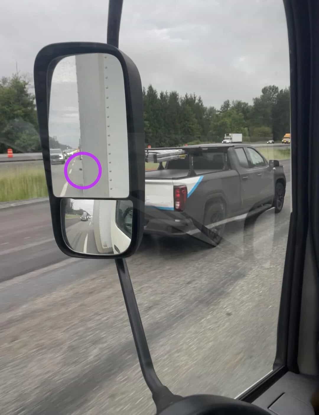 Black pickup truck with a blue stripe on the side, seen through a side mirror on a highway.