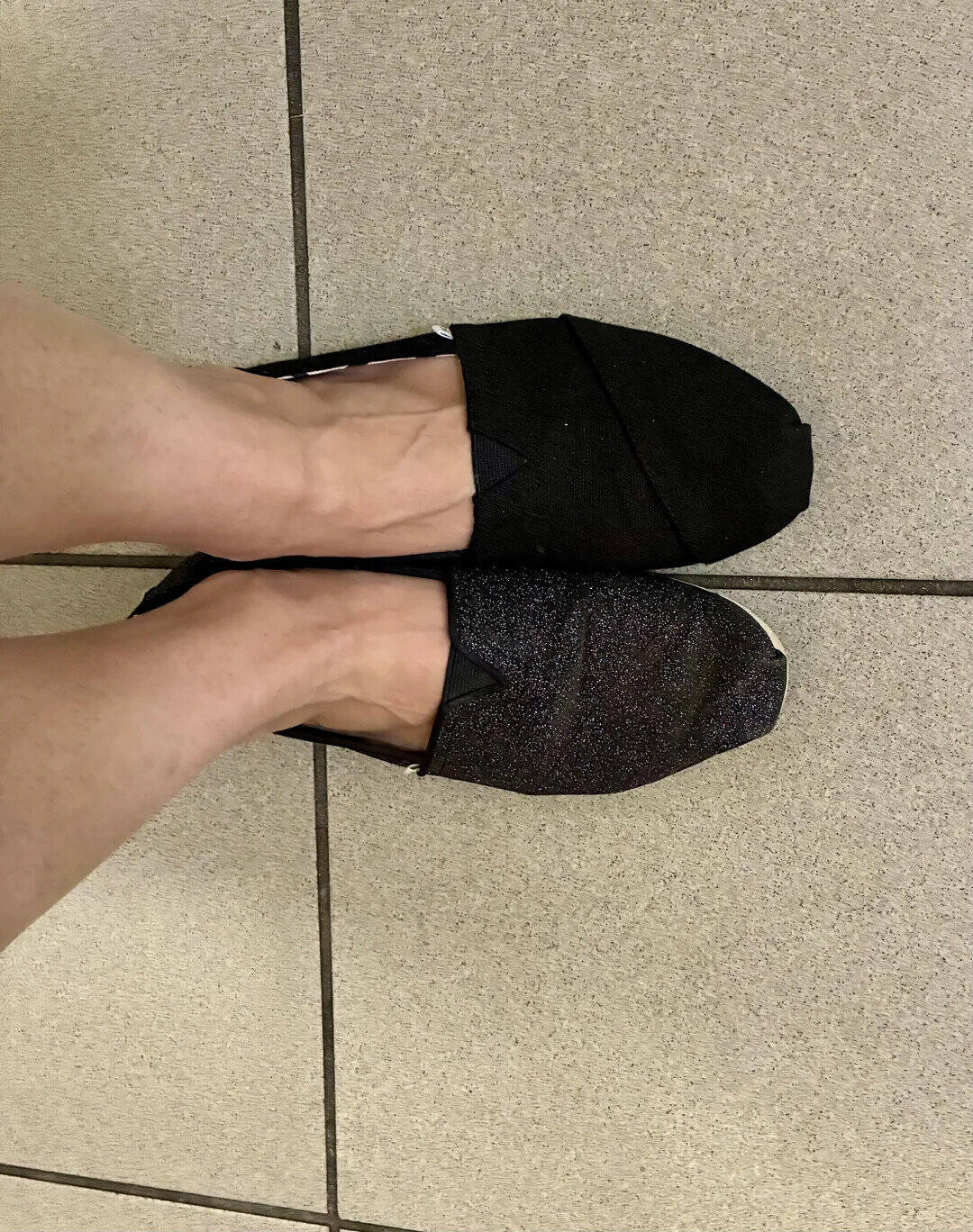Pair of black slippers on tiled floor, one slightly tilted.