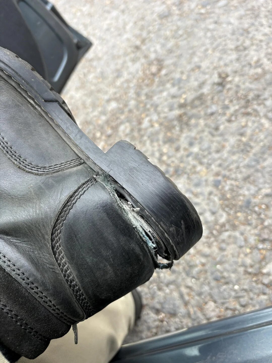 Worn-out black leather shoe with a damaged sole and frayed edge.
