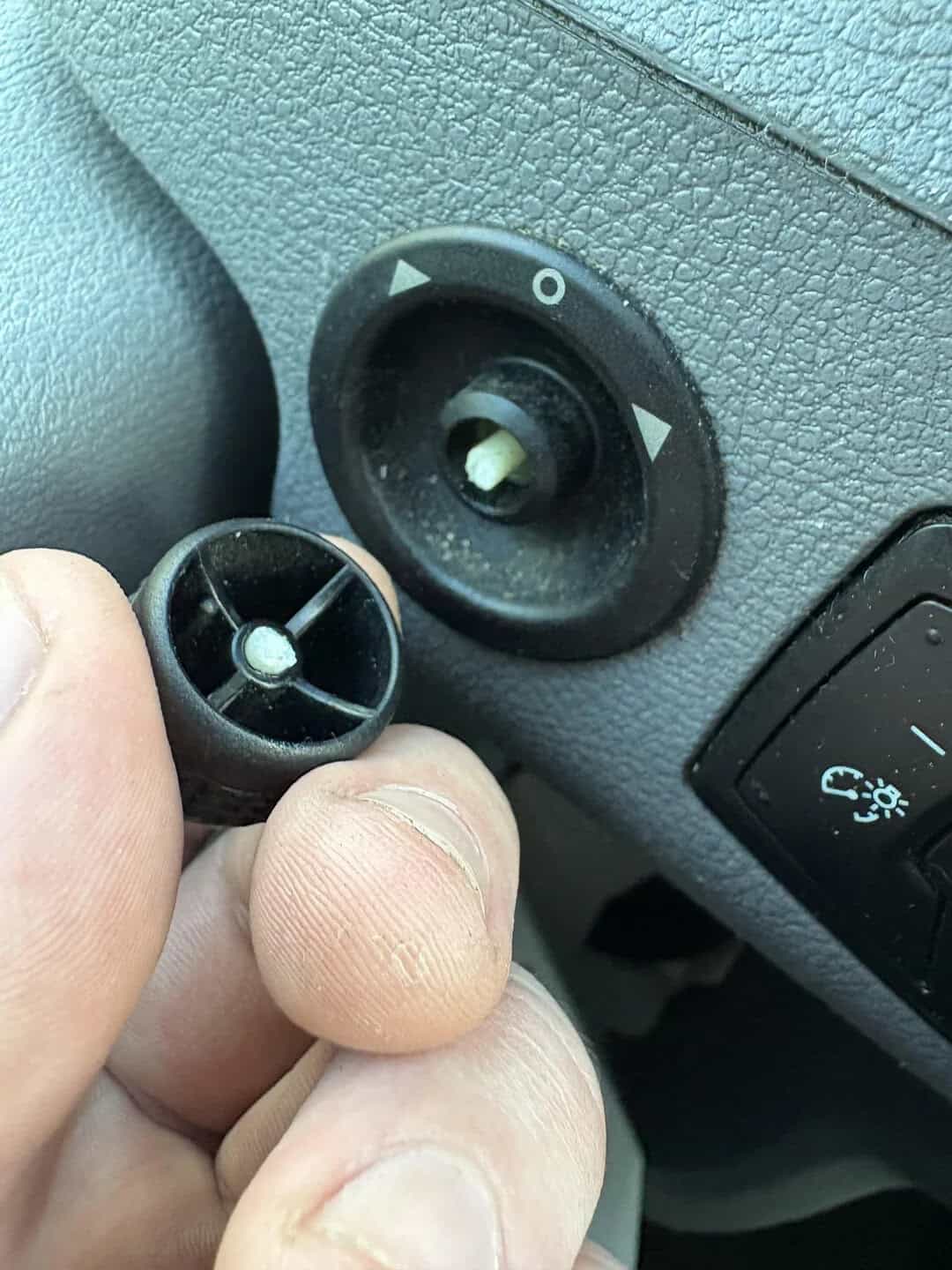 Person removing a circular black car part near a dashboard with a 0 and arrow symbols.