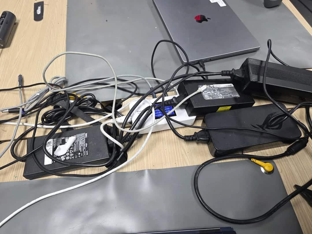 Messy desk with tangled cables, power adapters, and electronic devices.