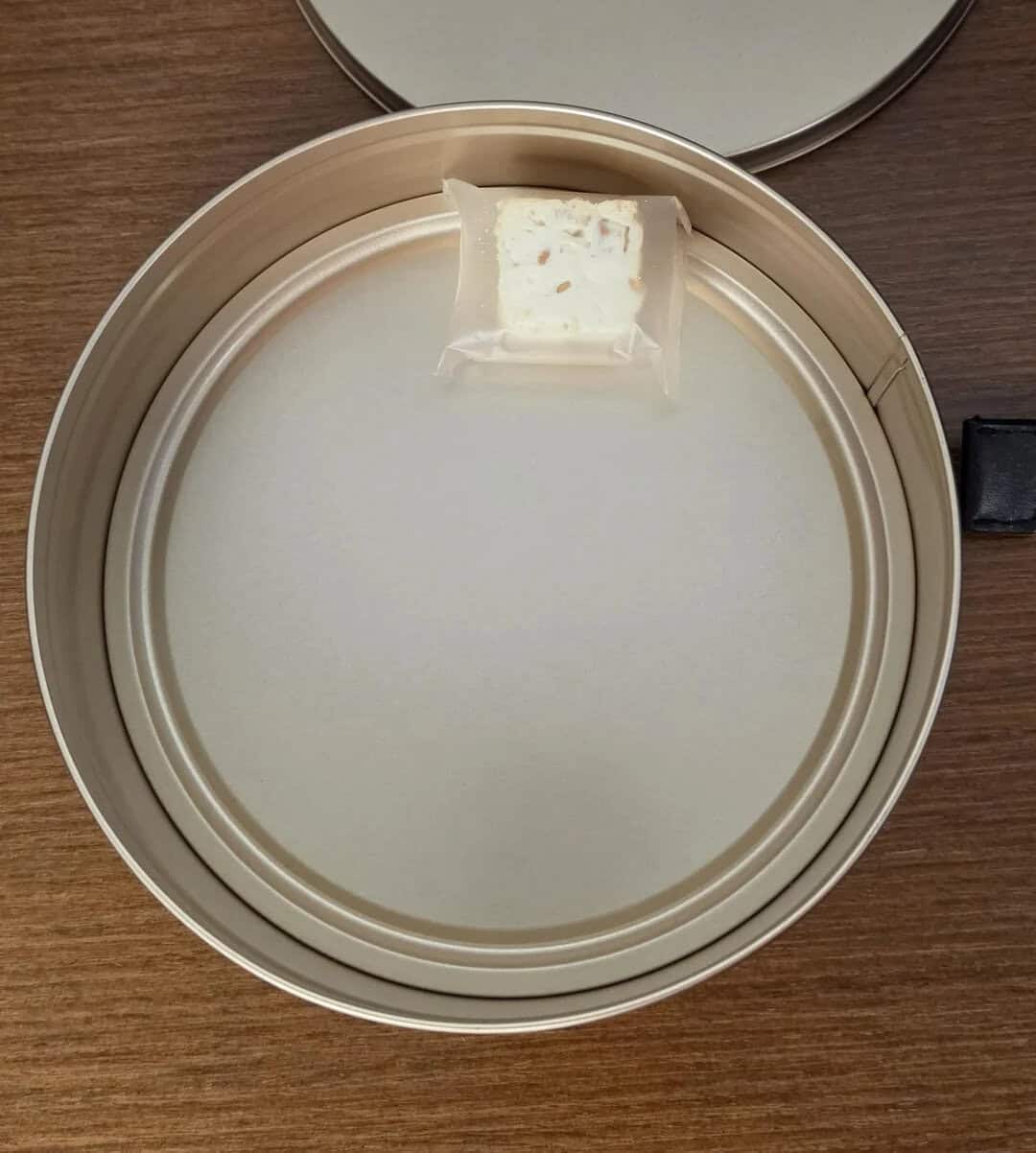 A small bar of soap in a plastic wrapper inside a round metal container.