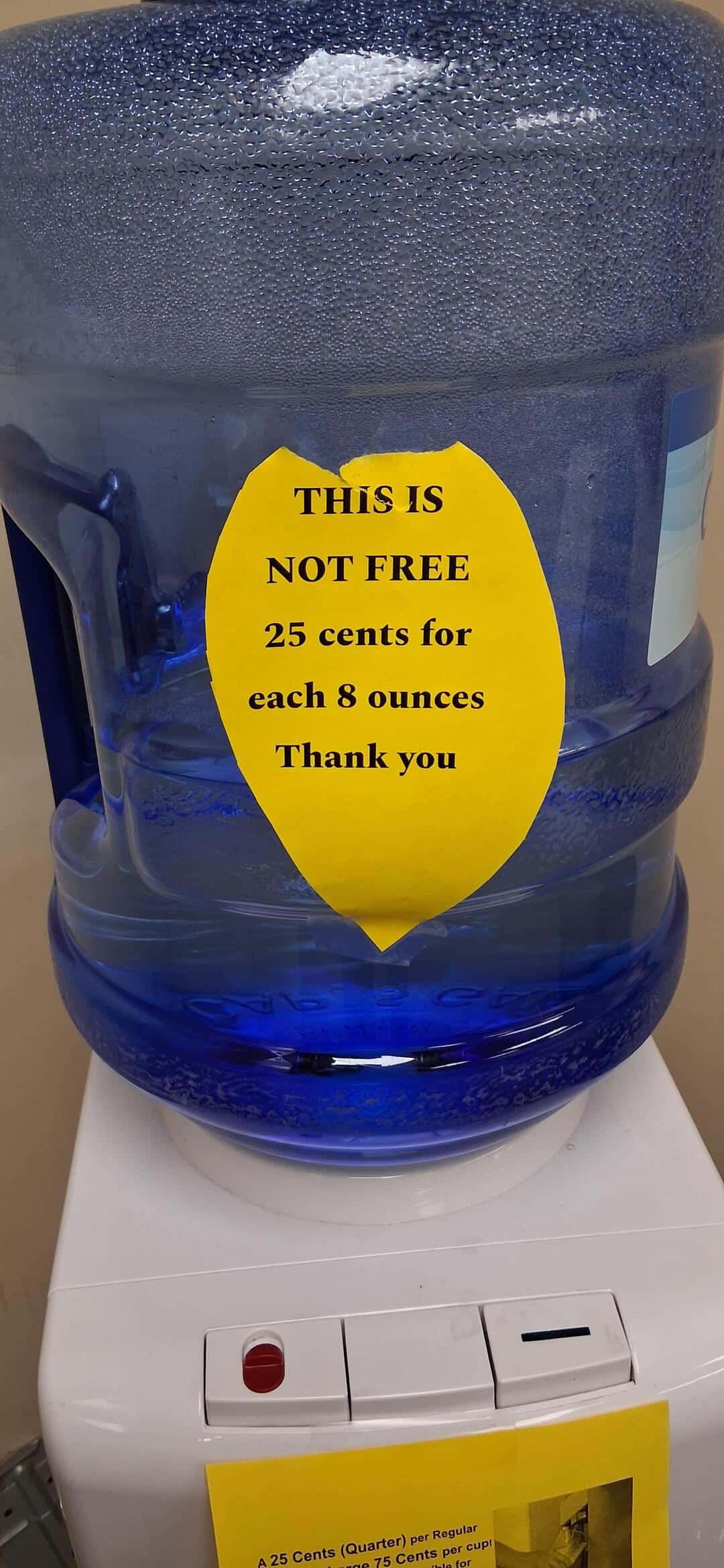 Water dispenser with a yellow sign saying 'This is not free, 25 cents for each 8 ounces, thank you'.