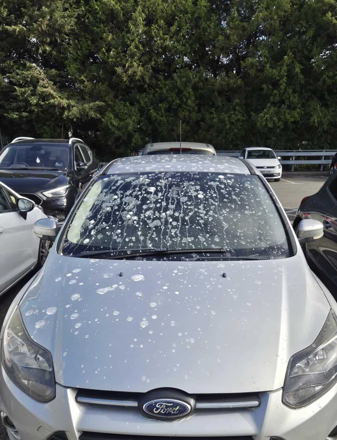 Silver Ford car with soap suds on windshield in parking lot.