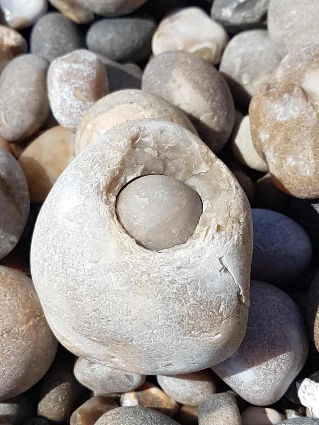 A large, smooth stone with a smaller stone inside a hollow in it, surrounded by other pebbles.