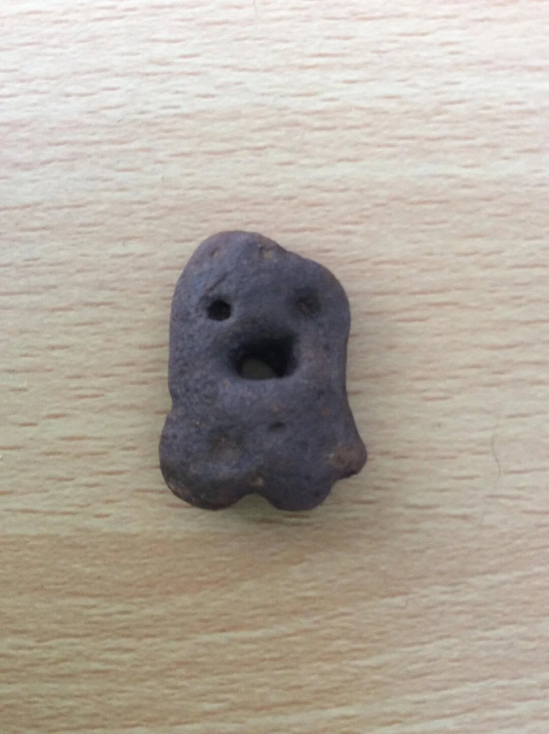 Small dark gray rock with face-like features on a wooden surface.