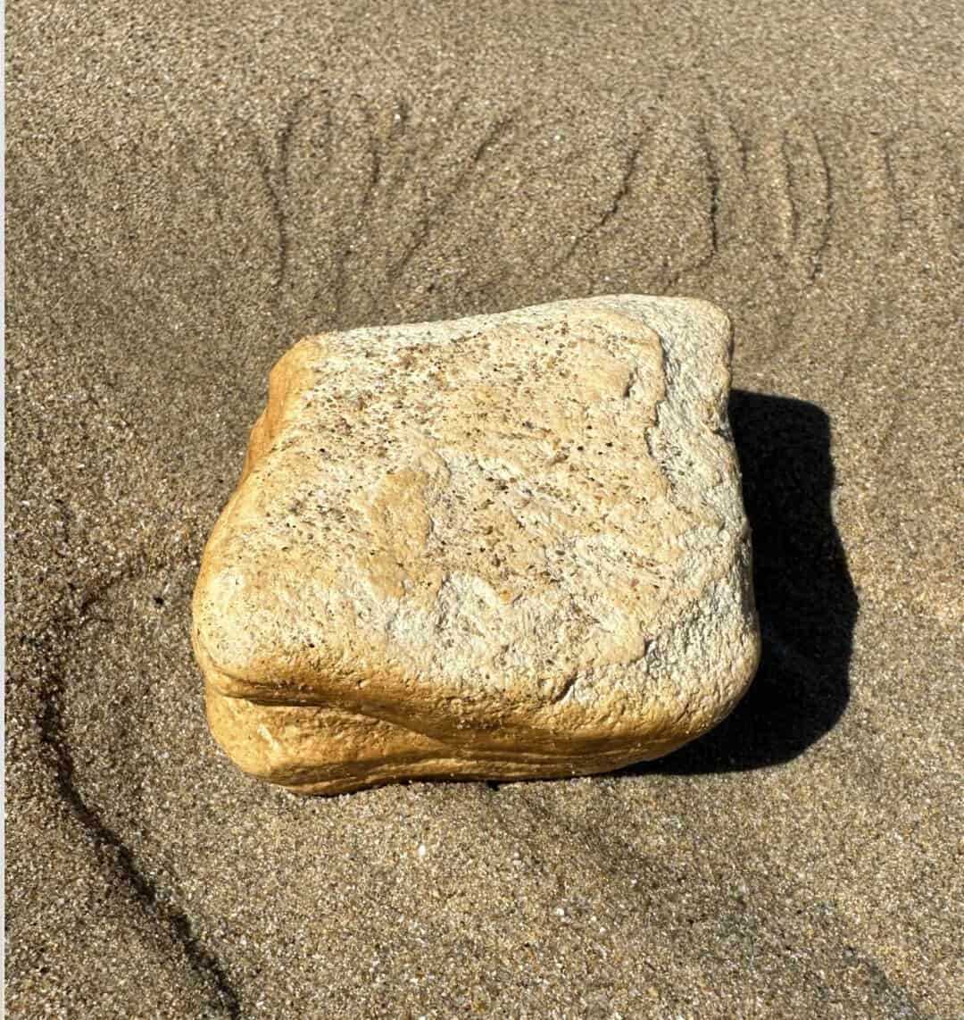 A large beige rock on sand with 'SAND' written above it in the sand.