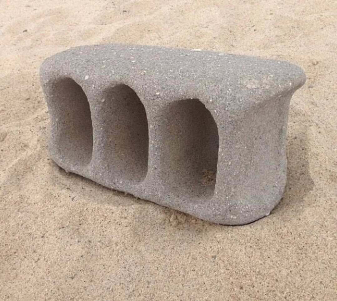 Concrete block with three hollow arches on a sandy beach.
