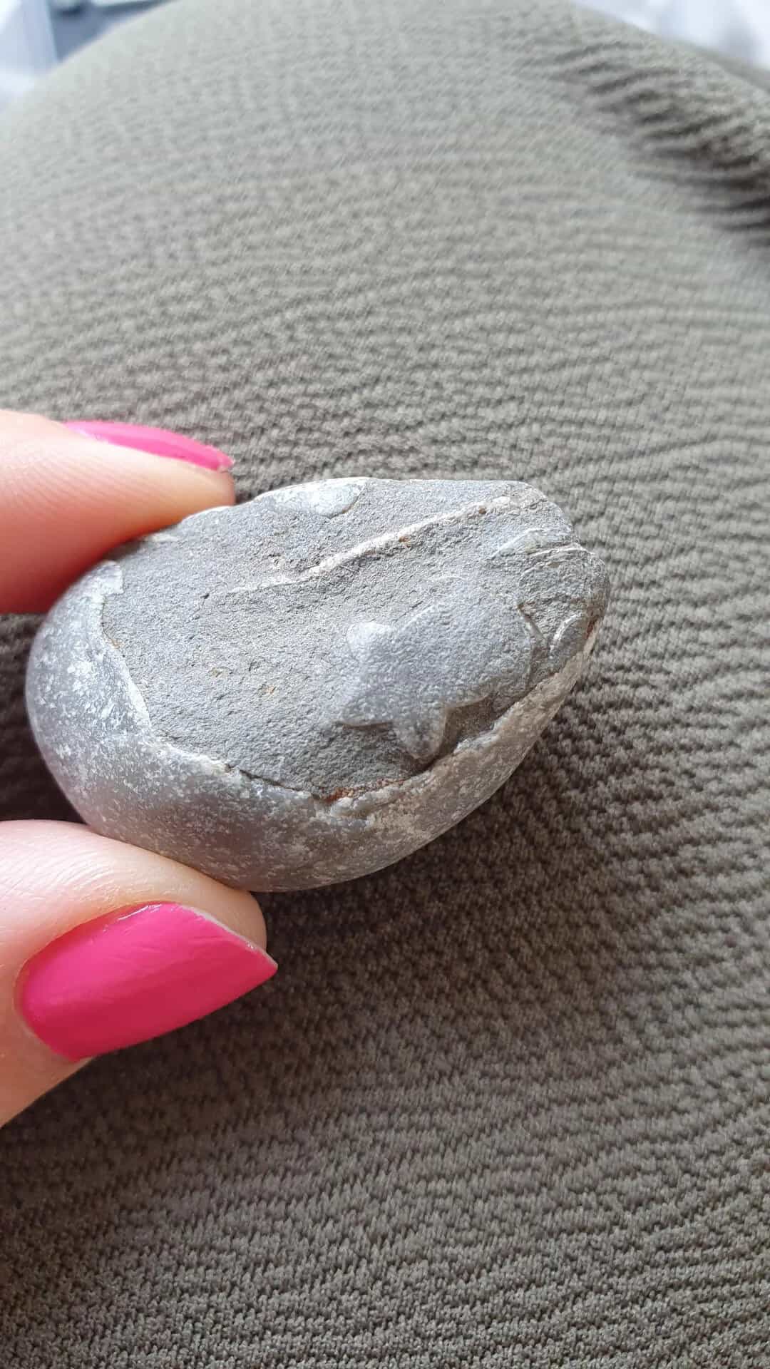Smooth gray pebble held between fingers on gray fabric background.