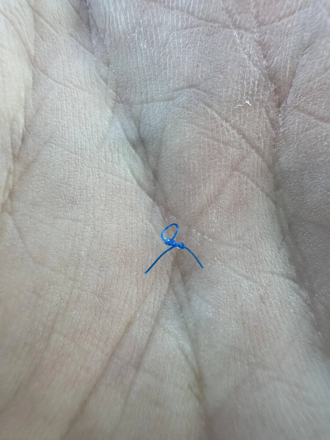Close-up of a hand with a small blue string tied in a knot.
