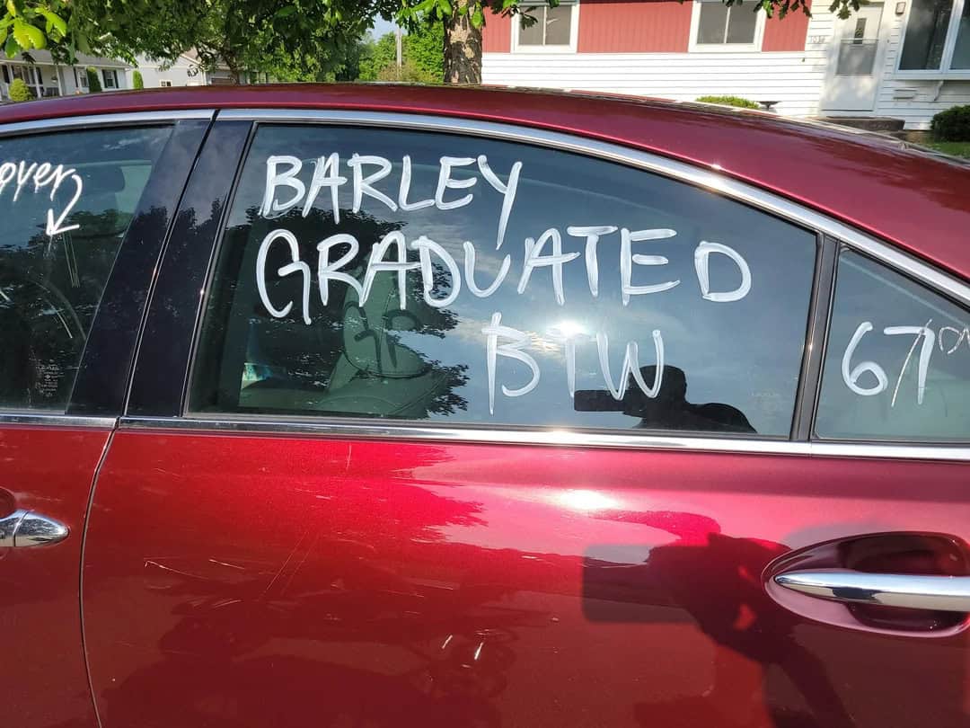 Graduated in BSW written on car window, red vehicle parked outdoors with trees and house in backgrou.
