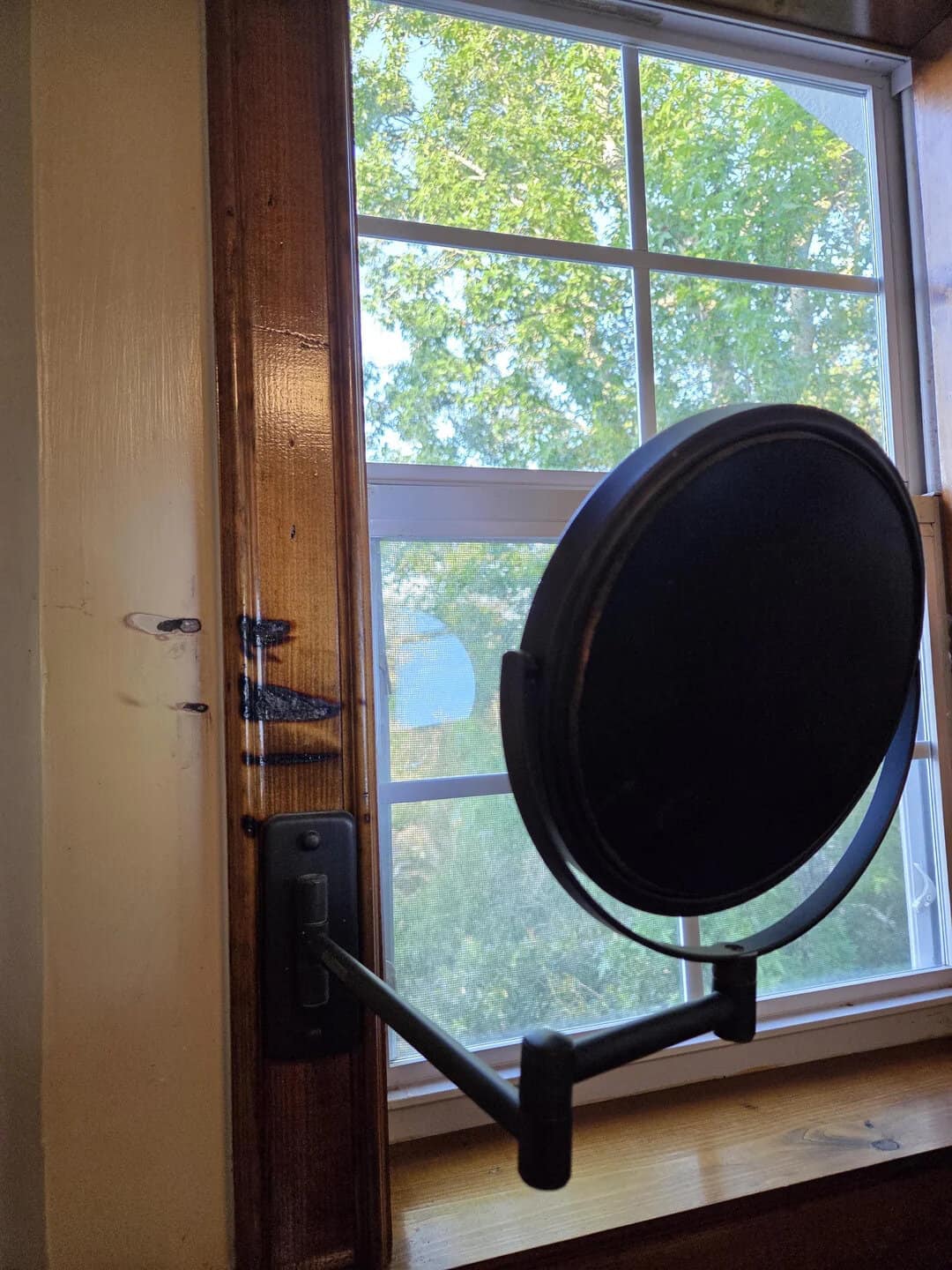 Window with a black microphone pop filter attached to a wooden wall.