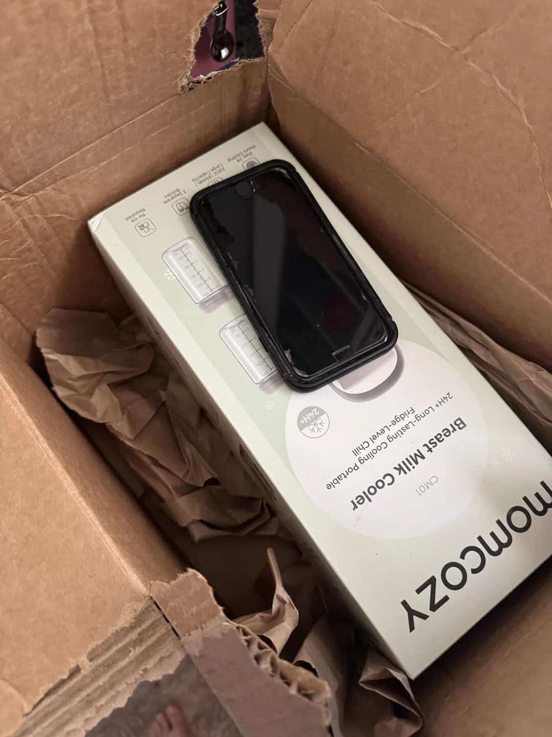 Smartphone on top of a boxed device inside a cardboard box.