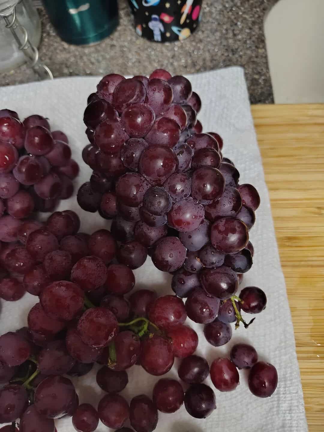 Bunch of red grapes on a paper towel on a kitchen counter.