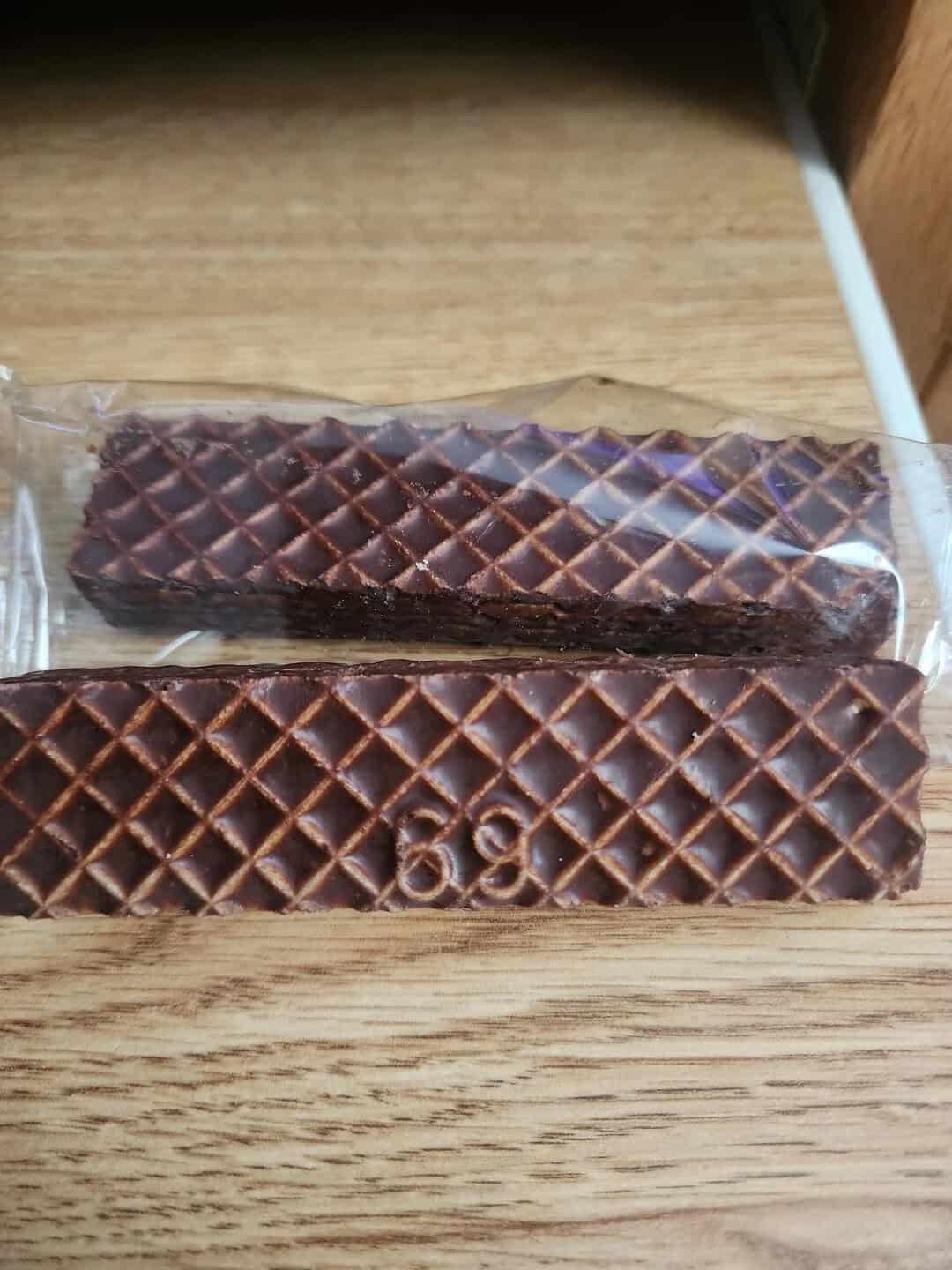 Chocolate wafer sticks in clear plastic wrapper, placed on a wooden surface.