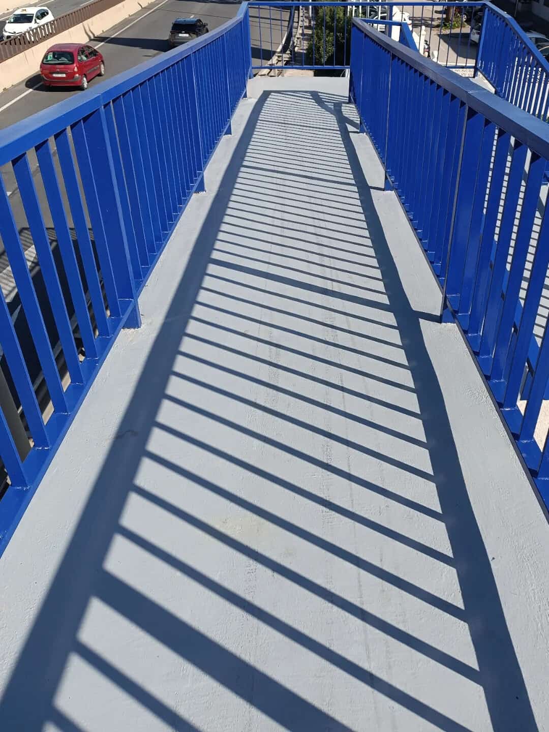Elevated walkway with blue railings and shadow patterns, outdoors.