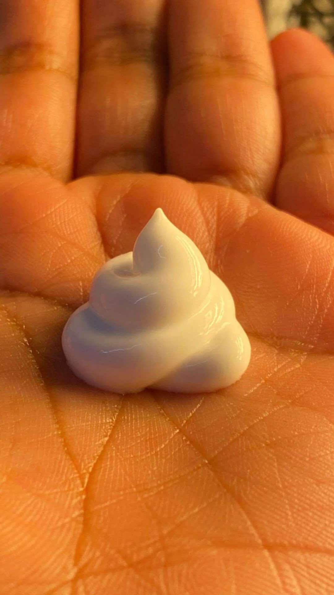 A dollop of white cream on a person's palm with fingers in the background.
