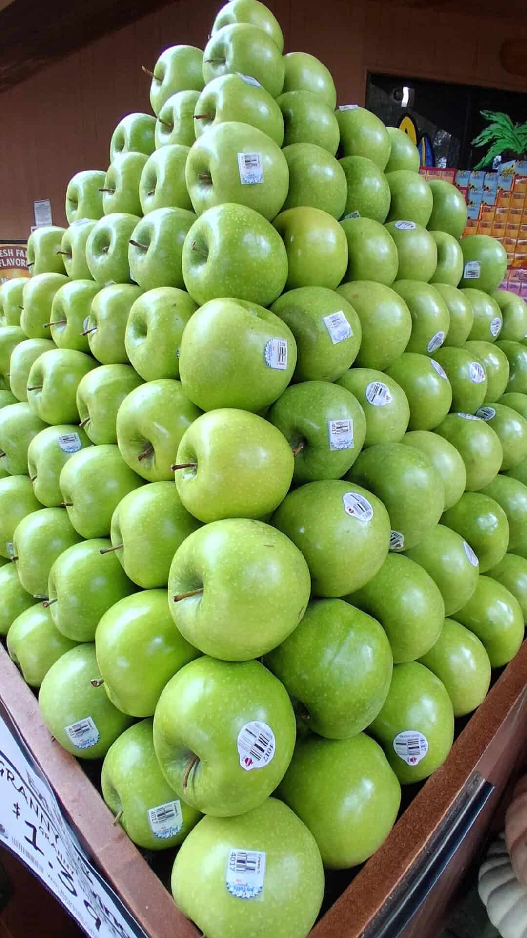 Green apples stacked in a pyramid display at a store.