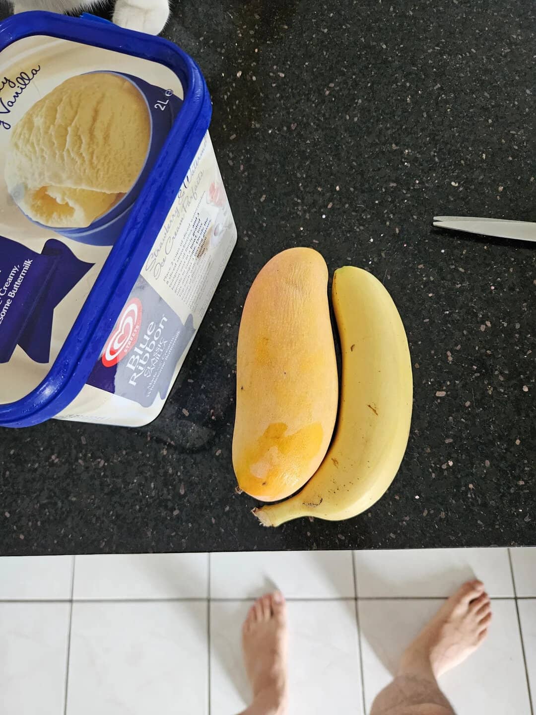 Bananas and ice cream on a black countertop with a pair of feet visible.