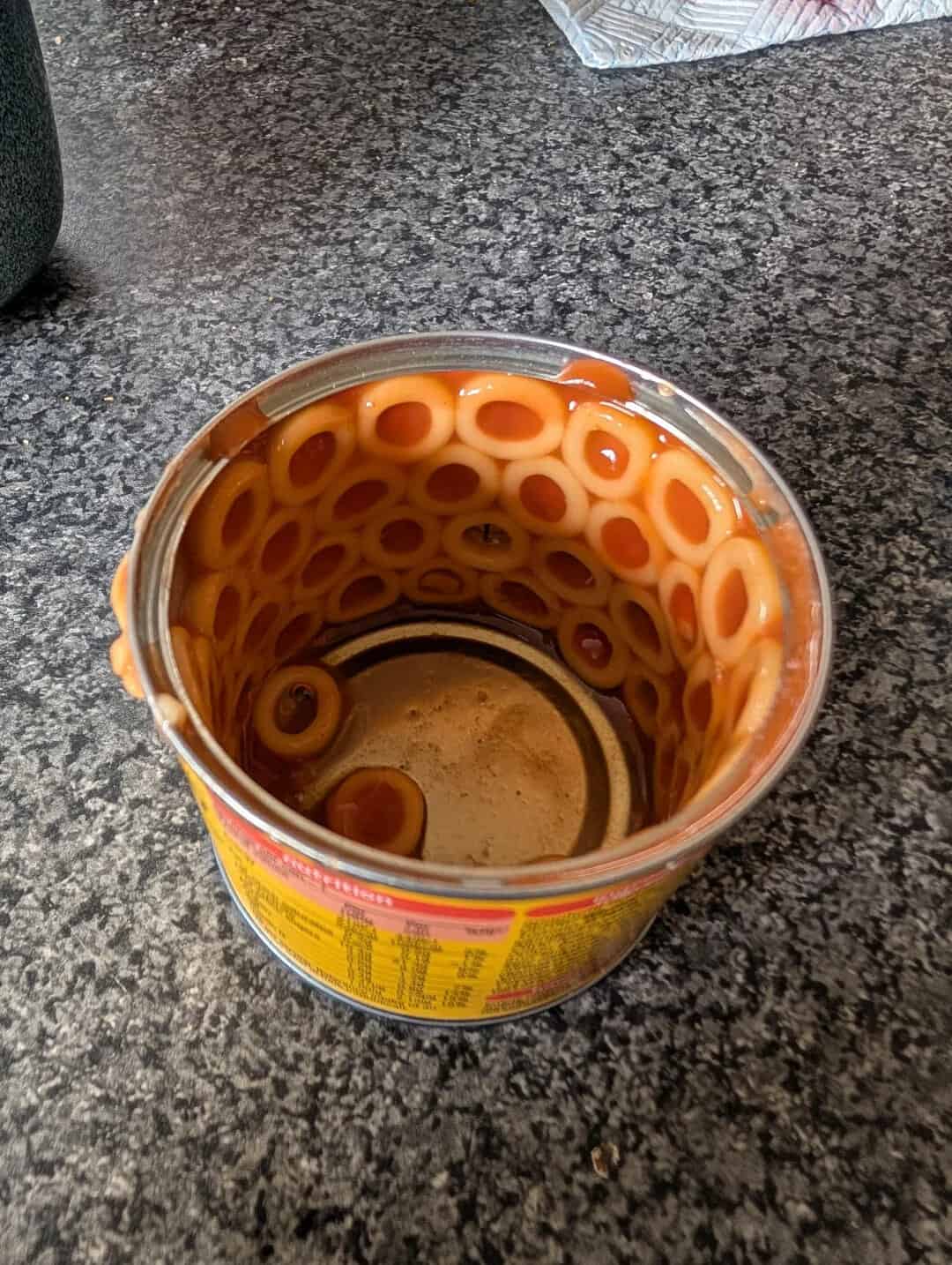 Empty instant noodle cup with some broth remaining, placed on a dark countertop.