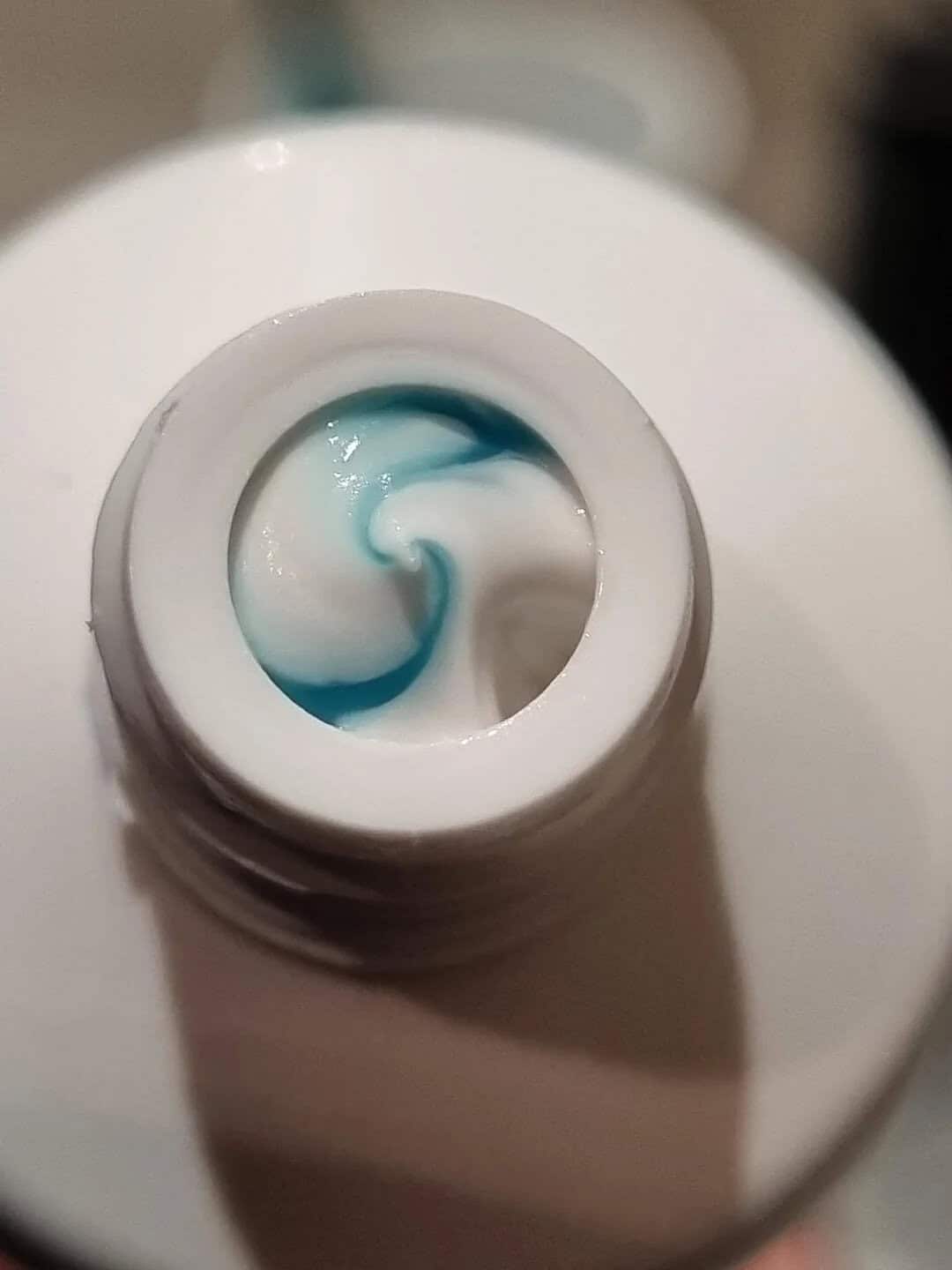 Toothpaste swirl with blue and white colors in an open tube.