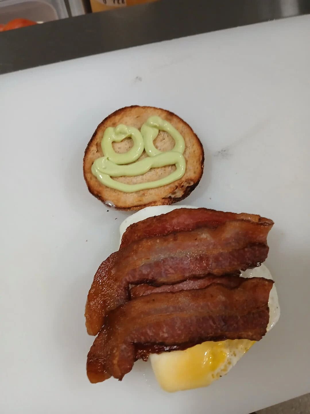 Bacon, egg, and toast with smiley face drawn in green sauce.