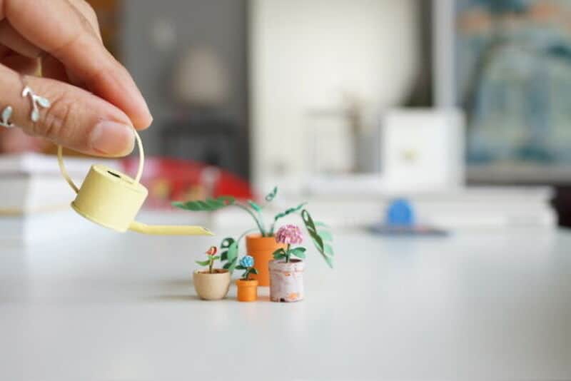 Miniature paper art of a garden scene with a watering can and potted plants.