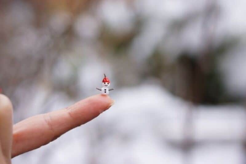 Miniature snowman on a finger with blurred snowy background.